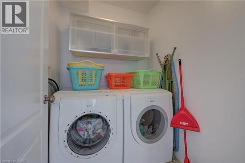 Dedicated laundry area featuring a front-loading washer and dryer, upper wall-mounted cabinetry, and a light-colored wall finish - 729 Keats Way, Waterloo, ON - Indoor Photo Showing Laundry Room
