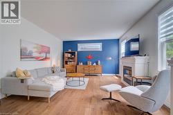 Bright living area featuring wood-finish flooring, a prominent white mantelpiece with an integrated fireplace, and windows with horizontal blinds - 