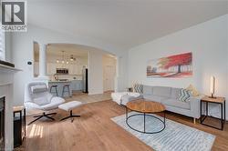 Open-concept living space featuring wood-finish flooring, white walls, an arched entryway, and a fireplace mantel - 
