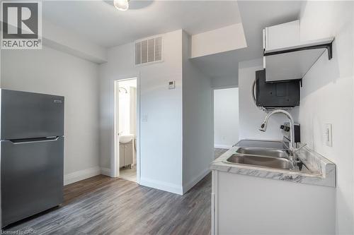 Compact kitchen featuring stainless steel appliances, wood-finish flooring, white cabinetry, a dual basin sink, and a countertop with a marble-style finish - 524 King Street E Unit# 3, Hamilton, ON - Indoor Photo Showing Kitchen With Double Sink
