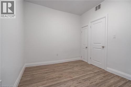 Neutral white walls featuring wood-finish flooring, white baseboards, and two paneled interior doors with silver-tone hardware - 524 King Street E Unit# 3, Hamilton, ON - Indoor Photo Showing Other Room