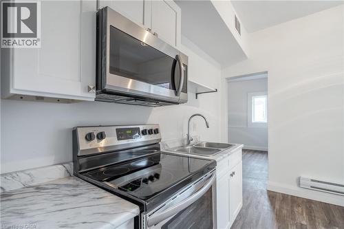 Kitchen featuring white cabinetry, stainless steel microwave, black electric range, dual basin stainless steel sink with a high-arc faucet, and wood-finish flooring - 524 King Street E Unit# 3, Hamilton, ON - Indoor Photo Showing Kitchen With Double Sink