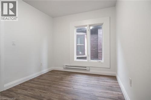 Bright room featuring wood-finish flooring, white walls, and a prominent window with white trim - 524 King Street E Unit# 3, Hamilton, ON - Indoor Photo Showing Other Room