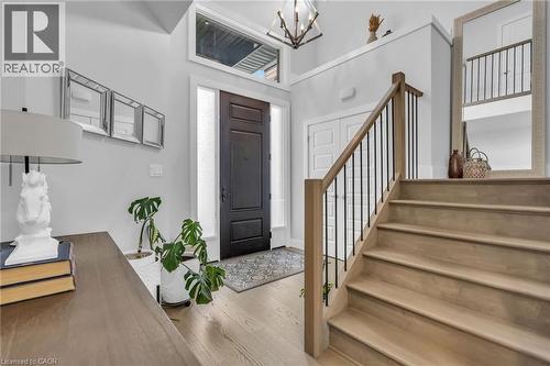 Entryway featuring a dark wood-finish door with sidelights and transom window, light wood-finish flooring, a contemporary chandelier, and a staircase with light wood-finish treads and black metal balu - 2195 Ironwood Road, London, ON - Indoor Photo Showing Other Room