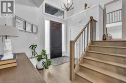 Entryway featuring a dark wood-finish door with sidelights and transom window, light wood-finish flooring, a contemporary chandelier, and a staircase with light wood-finish treads and black metal balu - 