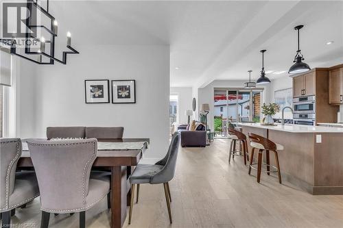 Open-concept living space featuring light wood-finish flooring, a contemporary dining area with a linear chandelier, and a kitchen island with pendant lighting - 2195 Ironwood Road, London, ON - Indoor Photo Showing Dining Room