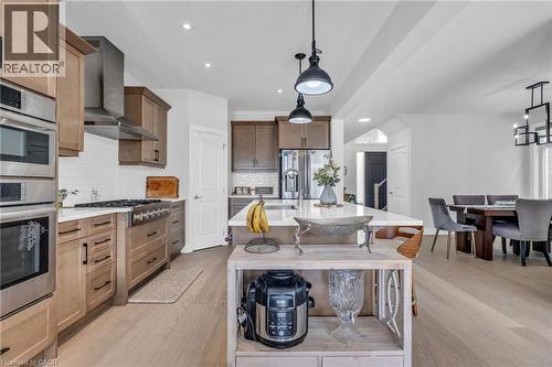 Bright, open-concept kitchen featuring a large central island with seating, stainless steel appliances including a double oven and range hood, two-tone cabinetry, and wood-finish flooring extending in - 2195 Ironwood Road, London, ON - Indoor Photo Showing Kitchen With Stainless Steel Kitchen With Upgraded Kitchen