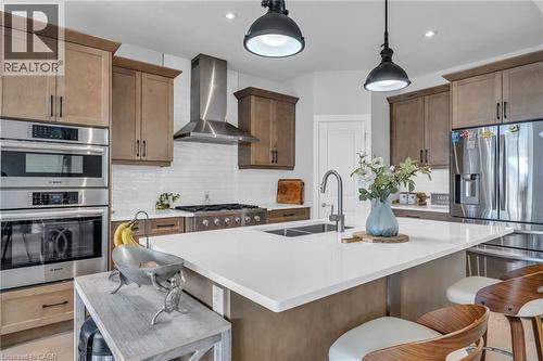 Modern kitchen featuring a large island with an undermount double sink, stainless steel appliances, a white subway tile backsplash, a gas range with a range hood, and wood-finish cabinetry - 2195 Ironwood Road, London, ON - Indoor Photo Showing Kitchen With Stainless Steel Kitchen With Double Sink With Upgraded Kitchen