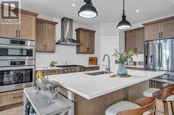 Modern kitchen featuring a large island with an undermount double sink, stainless steel appliances, a white subway tile backsplash, a gas range with a range hood, and wood-finish cabinetry - 