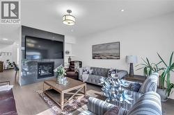 Spacious living area featuring light wood-finish flooring, a contemporary fireplace with a dark tile surround, and recessed lighting - 