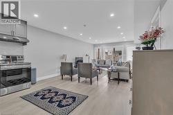 Open-concept living area featuring light wood-finish flooring, recessed lighting, light gray wall paint, and a kitchen area with stainless steel appliances and gray cabinetry - 