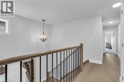 Upper level landing featuring wood-finish flooring, a contemporary chandelier, a staircase with wood handrails and black metal balusters, a window with white trim, and recessed lighting in the hallway - 2195 Ironwood Road, London, ON - Indoor Photo Showing Other Room