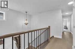 Upper level landing featuring wood-finish flooring, a contemporary chandelier, a staircase with wood handrails and black metal balusters, a window with white trim, and recessed lighting in the hallway - 