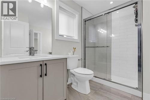 Modern bathroom featuring a glass-enclosed shower with subway tile surround, a single vanity with stone-look countertop, integrated sink, and brushed nickel faucet, and wood-finish tile flooring - 2195 Ironwood Road, London, ON - Indoor Photo Showing Bathroom