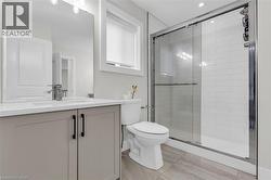 Modern bathroom featuring a glass-enclosed shower with subway tile surround, a single vanity with stone-look countertop, integrated sink, and brushed nickel faucet, and wood-finish tile flooring - 