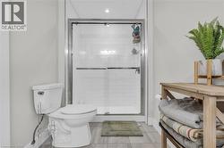 Modern bathroom featuring a glass-enclosed shower with subway tile surround, white toilet, and wood-finish flooring - 