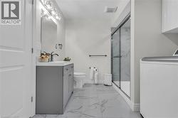Contemporary bathroom featuring a grey vanity with an integrated sink, a glass-enclosed shower with marble-look wall tiling, a toilet, and large-format marble-look floor tiles - 