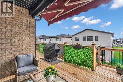 Expansive outdoor deck featuring wood-finish flooring, a brick exterior wall, a retractable awning, and black metal railings with wood posts - 2195 Ironwood Road, London, ON - Outdoor With Deck Patio Veranda With Exterior