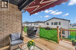 Expansive outdoor deck featuring wood-finish flooring, a brick exterior wall, a retractable awning, and black metal railings with wood posts - 