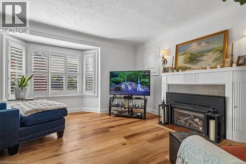 Living area featuring wood-finish flooring, a bay window with white plantation shutters, a decorative fireplace with a mantel, and wall sconces - 573 Beach Boulevard, Hamilton, ON - Indoor Photo Showing Living Room With Fireplace
