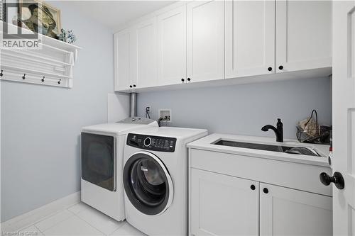 Laundry area featuring white shaker-style cabinetry, a white countertop with an integrated sink, a matte black faucet, and white tile flooring - 573 Beach Boulevard, Hamilton, ON - Indoor Photo Showing Laundry Room