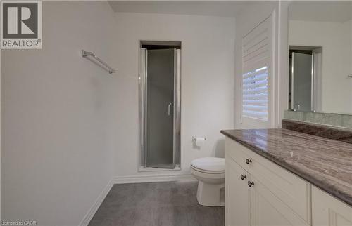 Bathroom featuring a glass-enclosed shower, white toilet, single vanity with a stone countertop, white cabinetry with dark hardware, and gray wood-finish flooring - 52 Pointer Street, Cambridge, ON - Indoor Photo Showing Bathroom