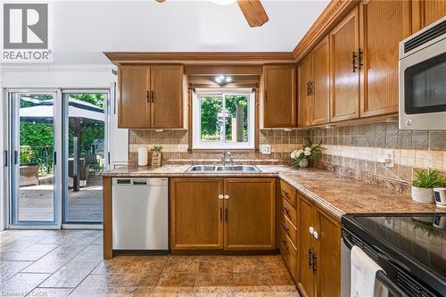 Kitchen featuring wood cabinetry, a stainless steel double basin sink, and a multi-toned tile backsplash - 34 Peachtree Crescent, Cambridge, ON - Indoor Photo Showing Kitchen With Double Sink