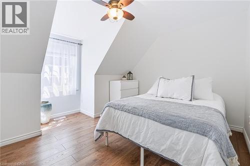 Attic room featuring sloped ceilings, wood-finish flooring, a window with sheer curtains, a ceiling fan with light fixture, and white painted walls - 34 Peachtree Crescent, Cambridge, ON - Indoor Photo Showing Bedroom