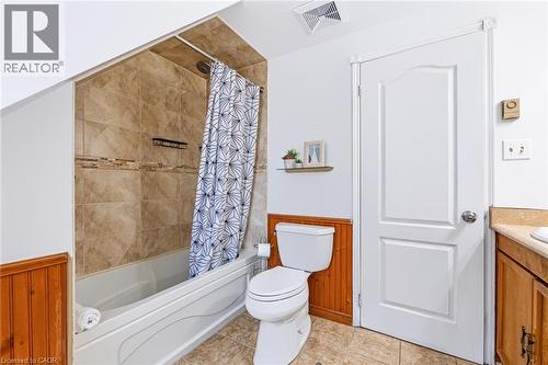 Bathroom featuring a white tub with tile surround, a built-in shower niche, wood paneling, a white toilet, and a vanity with a countertop - 34 Peachtree Crescent, Cambridge, ON - Indoor Photo Showing Bathroom