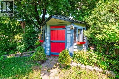 Garden shed featuring light blue siding with dark trim, a red Dutch door, and two small windows with flower boxes - 34 Peachtree Crescent, Cambridge, ON - Outdoor