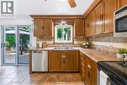 Kitchen featuring wood cabinetry, a stainless steel double basin sink, and a multi-toned tile backsplash - 