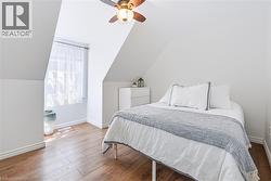 Attic room featuring sloped ceilings, wood-finish flooring, a window with sheer curtains, a ceiling fan with light fixture, and white painted walls - 