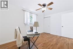 Bright room featuring wood-finish flooring, a window with white sheer curtains, a ceiling fan with integrated lighting, and white walls - 
