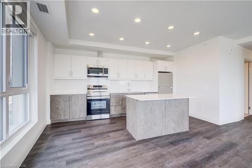 Modern kitchen featuring sleek white upper cabinetry, wood-finish lower cabinetry, and stainless steel appliances - 1333 Weber Street E Unit# 708, Kitchener, ON - Indoor Photo Showing Kitchen