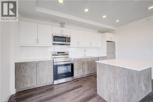 Contemporary kitchen featuring white upper cabinetry, wood-finish lower cabinetry, a center island with a white countertop, stainless steel appliances, and wood-finish flooring - 1333 Weber Street E Unit# 708, Kitchener, ON - Indoor Photo Showing Kitchen