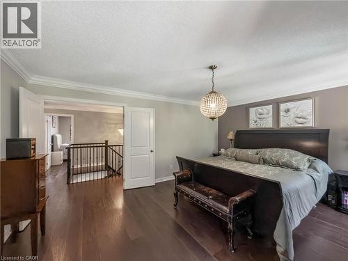 Spacious primary bedroom showcasing dark wood-finish flooring, a black upholstered bed frame, crown molding throughout, and a decorative pendant light fixture - 80 Sutherland Crescent, Ancaster, ON - Indoor Photo Showing Bedroom
