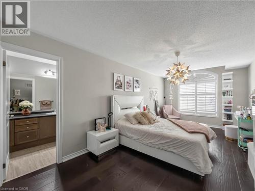 Spacious room featuring dark wood-finish flooring, a decorative ceiling light fixture, and a large window with white plantation shutters - 80 Sutherland Crescent, Ancaster, ON - Indoor Photo Showing Bedroom