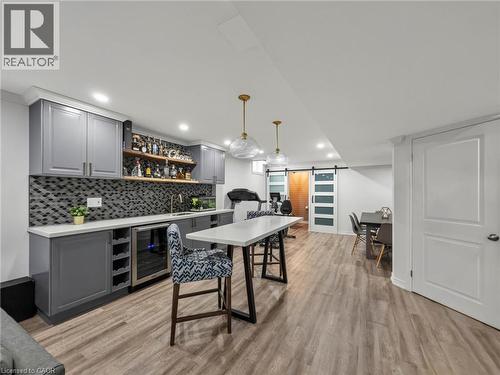 Spacious lower-level entertainment area featuring wood-finish flooring, a built-in wet bar with gray cabinetry, a mosaic tile backsplash, and a beverage refrigerator - 80 Sutherland Crescent, Ancaster, ON - Indoor