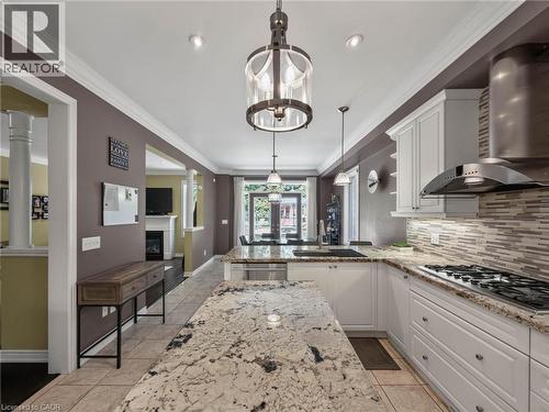 Sophisticated kitchen featuring white cabinetry, a sprawling quartz-topped island with waterfall edge, stainless steel gas range and hood, subway tile backsplash, and recessed lighting throughout - 80 Sutherland Crescent, Ancaster, ON - Indoor