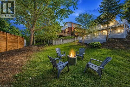 Expansive backyard oasis featuring a manicured lawn, mature landscaping with established trees, a built-in fire pit seating area with Adirondack chairs, and professional hardscaping - 23 Aberdeen Street, Caledonia, ON - Outdoor