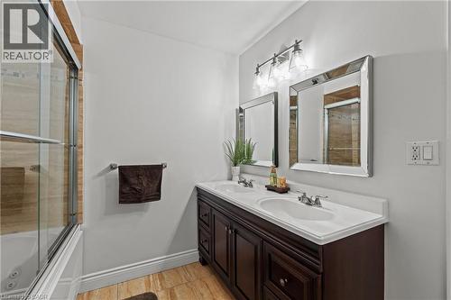 Bathroom with wood-finish flooring, a dual vanity with a white countertop and undermount sinks, two framed mirrors, and an overhead three-light fixture - 167 Berkindale Drive, Hamilton, ON - Indoor Photo Showing Bathroom