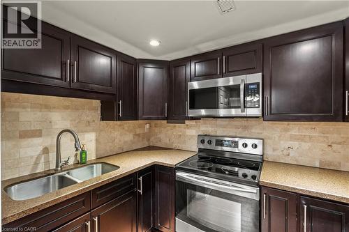 Kitchen featuring dark wood cabinetry, a stainless steel double-basin sink with a gooseneck faucet, light-toned stone tile backsplash, and composite countertops - 167 Berkindale Drive, Hamilton, ON - Indoor Photo Showing Kitchen With Double Sink