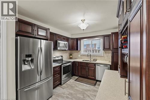 Kitchen featuring rich wood cabinetry, stainless steel appliances, light-toned countertops, and a tile backsplash - 167 Berkindale Drive, Hamilton, ON - Indoor Photo Showing Kitchen With Double Sink With Upgraded Kitchen