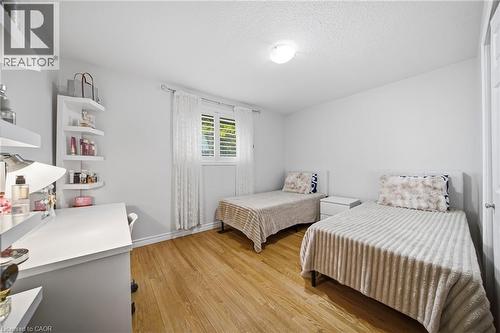 Bright secondary bedroom featuring wood-finish flooring, two twin beds with coordinating striped bedding, a dedicated work desk with storage shelving, and abundant natural light from a shuttered windo - 6346 Neuchatel Road, Mississauga, ON - Indoor Photo Showing Bedroom