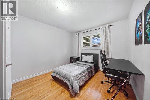 Comfortable bedroom featuring warm wood-finish flooring, a single bed with upholstered headboard, and a dedicated workspace with black desk and ergonomic chair - 6346 Neuchatel Road, Mississauga, ON - Indoor Photo Showing Bedroom