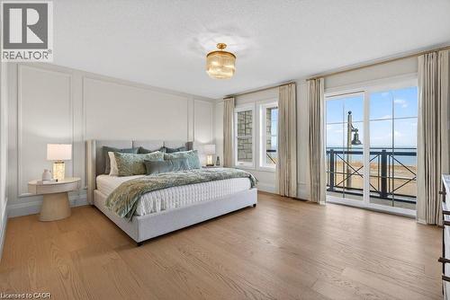 Wood-finish flooring, wall paneling, built-in ceiling light fixture, and sliding glass doors to a balcony - 100 Watershore Drive Unit# 15, Hamilton, ON - Indoor Photo Showing Bedroom