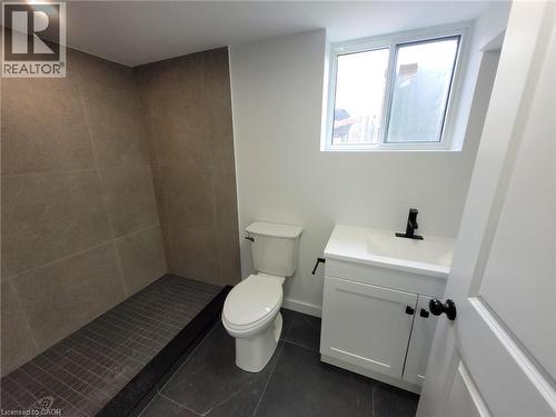 Bathroom featuring a walk-in shower with tile surround, white vanity with integrated sink, matte black faucet, and dark tile flooring - 132 East 31St Street, Hamilton, ON - Indoor Photo Showing Bathroom