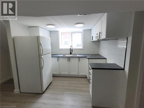 Renovated kitchen featuring white cabinetry with black countertops, subway tile backsplash, stainless steel appliances including refrigerator and range, recessed ceiling lighting, and wood-finish floo - 132 East 31St Street, Hamilton, ON - Indoor Photo Showing Kitchen