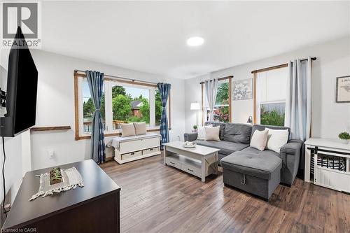 Bright and spacious living room featuring wood-finish flooring, multiple large windows with natural light, a gray upholstered sectional sofa, glass-top coffee table, wall-mounted flat-screen televisio - 450 East 42Nd Street, Hamilton, ON - Indoor Photo Showing Living Room