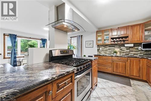 Chef's kitchen featuring custom wood cabinetry with glass-front upper storage, granite countertops, a professional-grade gas range with stainless steel hood, and a large island with additional prep sp - 450 East 42Nd Street, Hamilton, ON - Indoor Photo Showing Kitchen